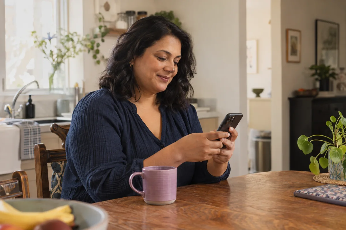 A woman using her phone at her kitchen table — an illustration of chat-based care at home